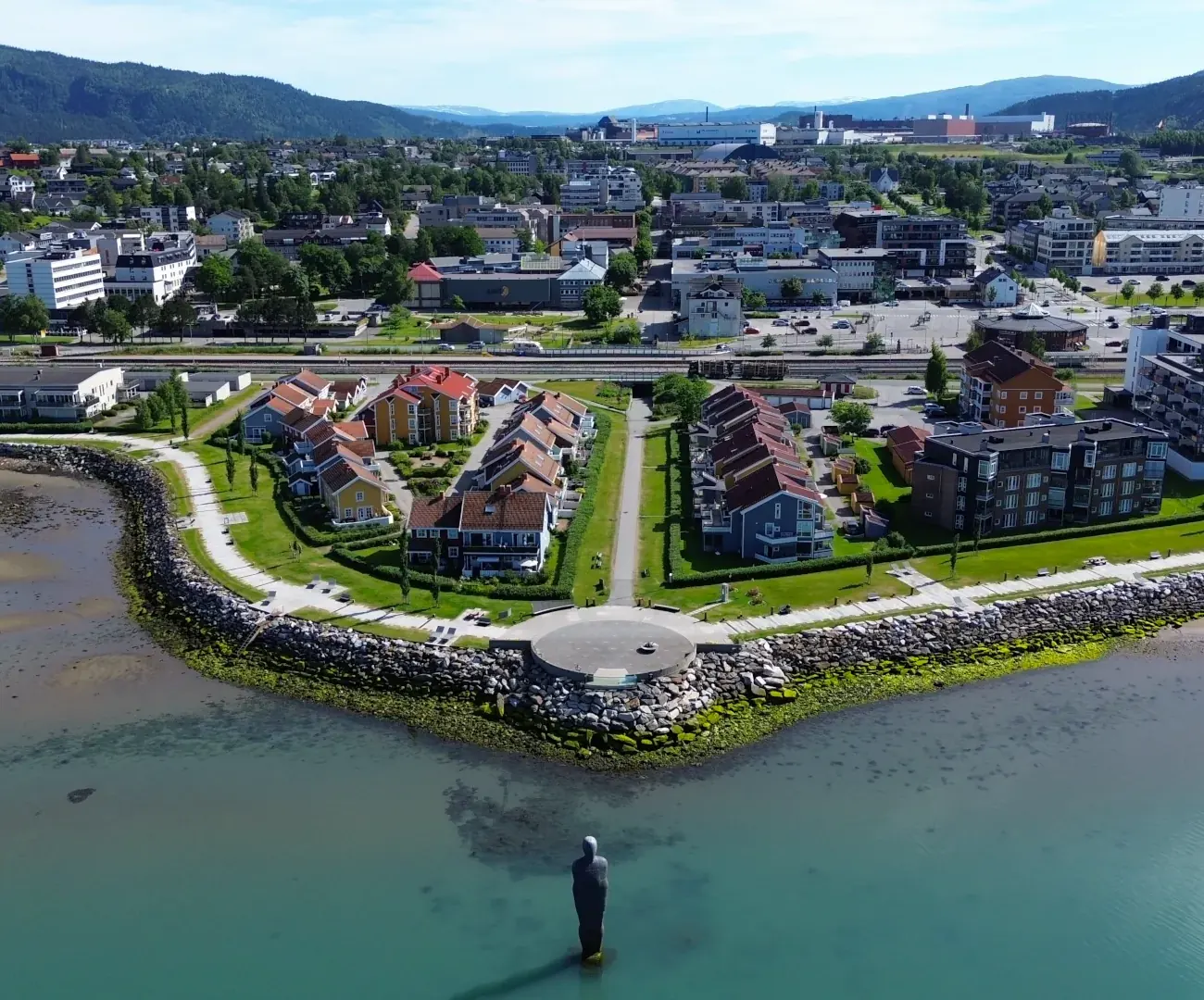 Mo i Rana sett fra lufta en sommerdag, med Havmannen-statuen ute i fjorden