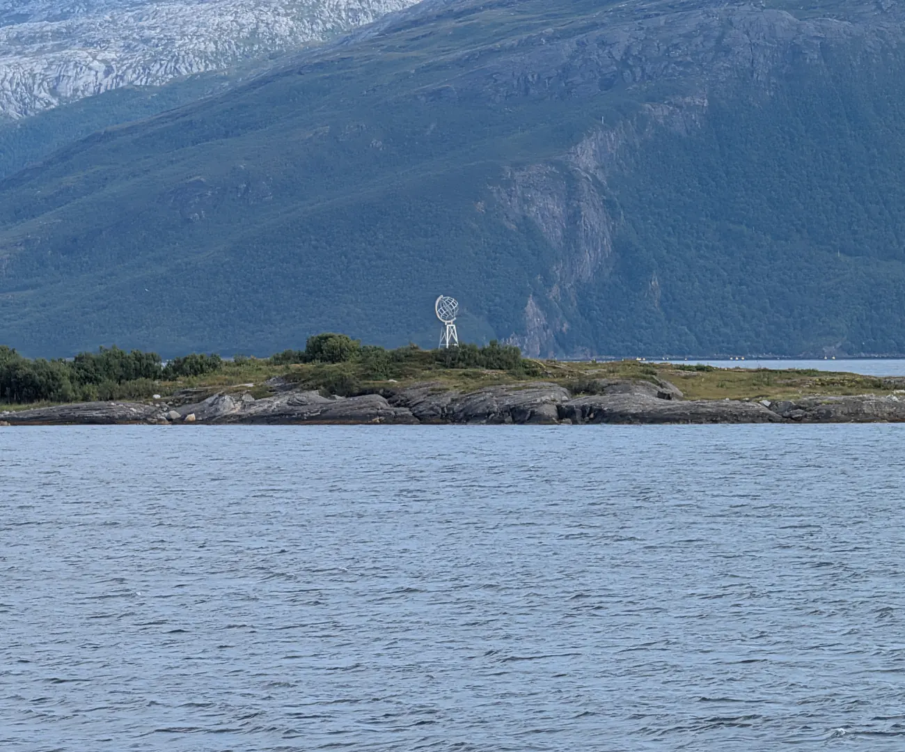 Polarsirkel-globusen på en lav, steinete holme i havet, med bratte, grønne fjell bak