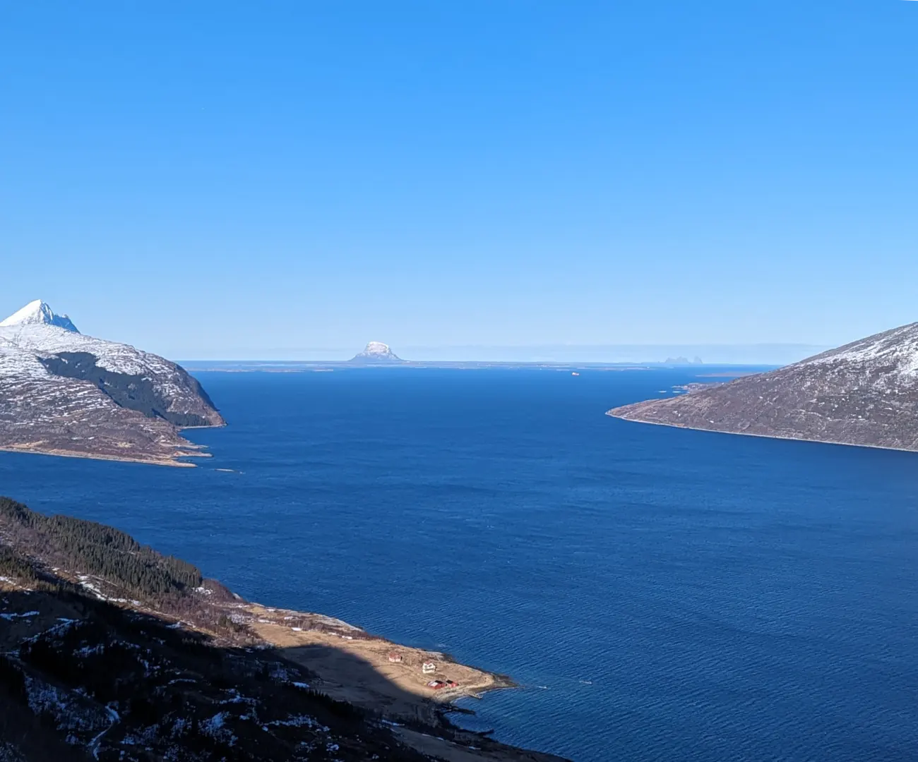 Utsikt fra Sjonfjellet mot øyriket, over en dyp blå fjord mellom snødekte fjell under en klar himmel