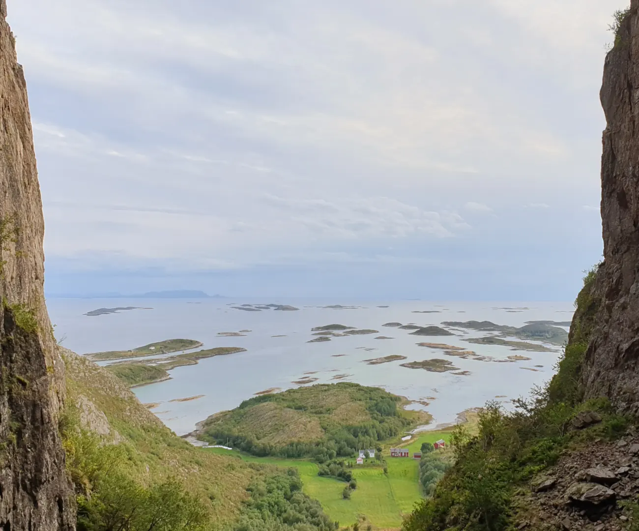 Utsikt gjennom hullet i Torghatten ved Brønnøysund, med bratte fjellvegger på hver side, grønne jorder nedenfor og havet fullt av små øyer